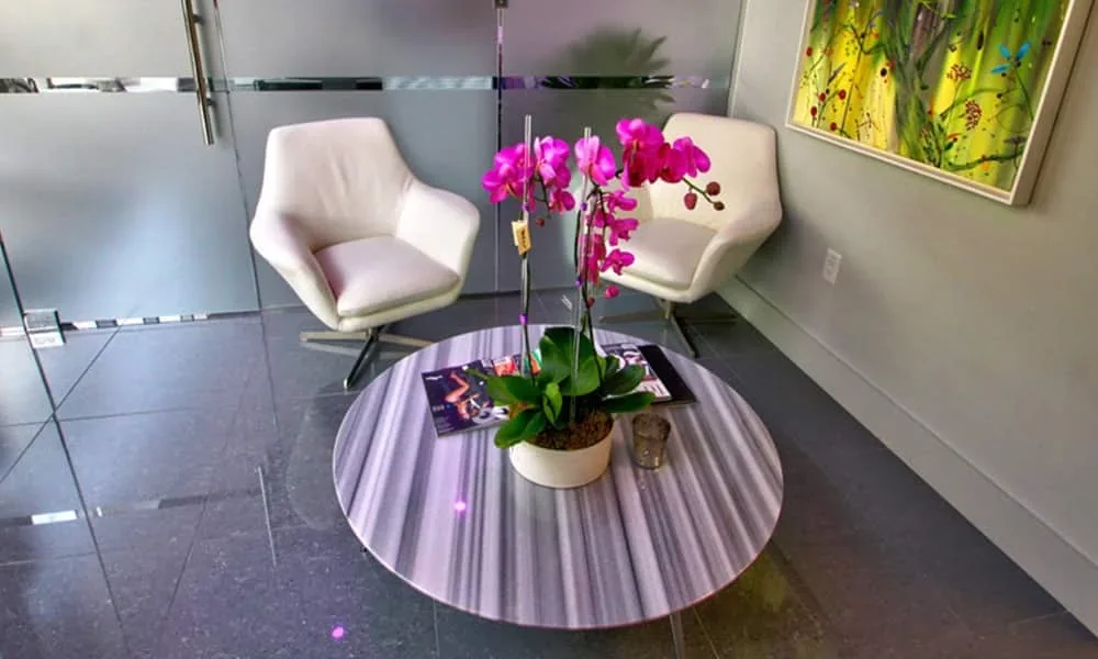 White armchairs and an orchid table beside a glass partition.