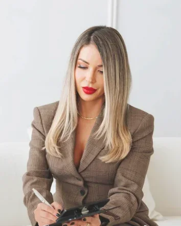 Yuni Medina wearing a checked jacket and holding a clipboard against a light background.