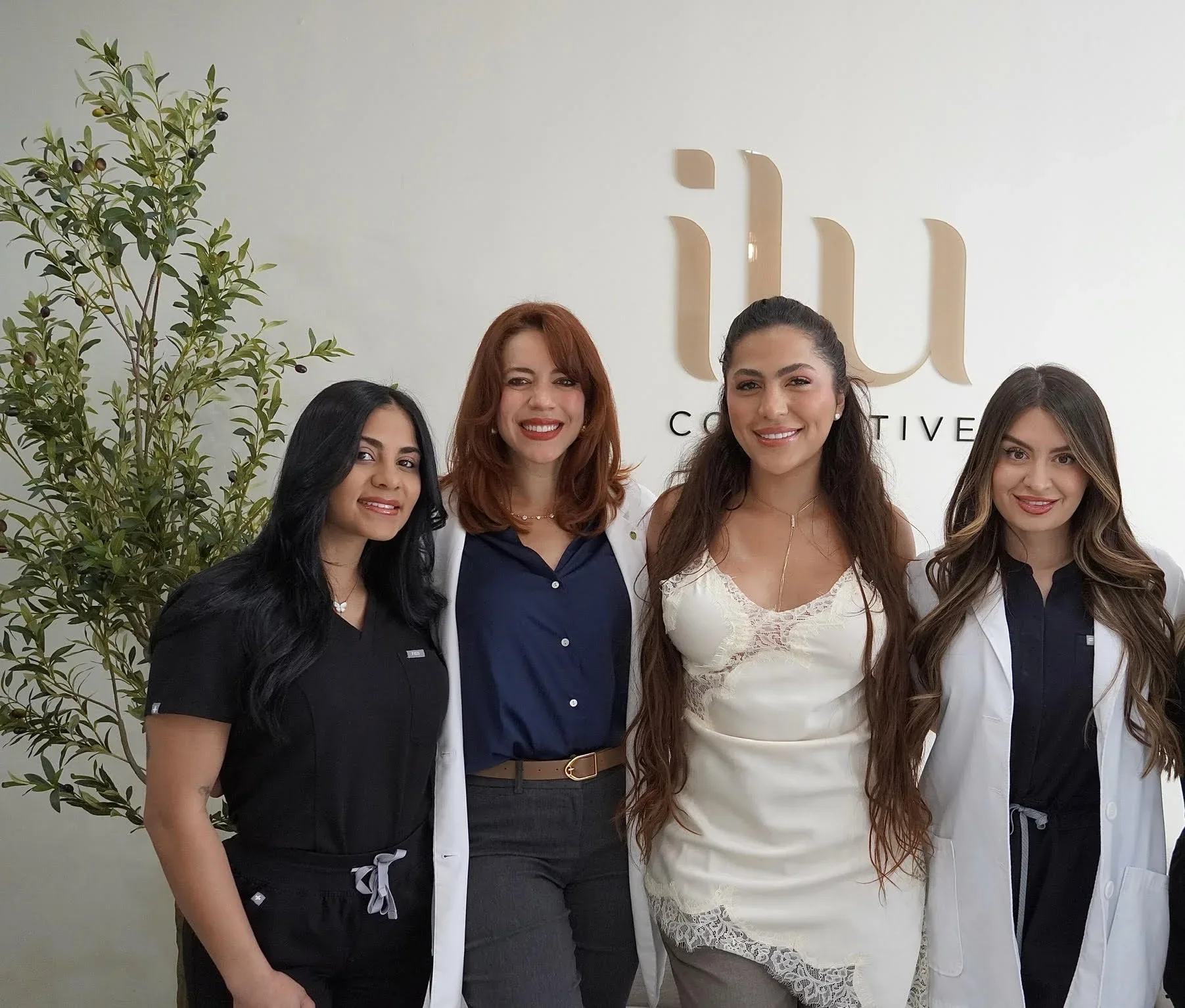 Four team members posed in front of the ILU Collective sign and a plant.