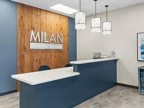 Empty blue reception counter beneath Milan branding, a wood wall and pendant lights.