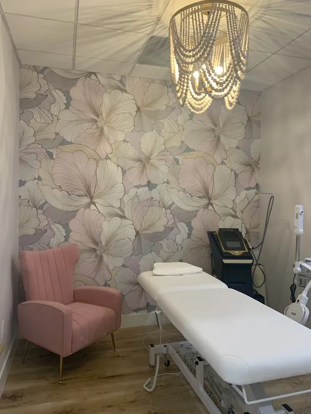 Empty room with floral wallpaper, pink chair and a white covered bed.