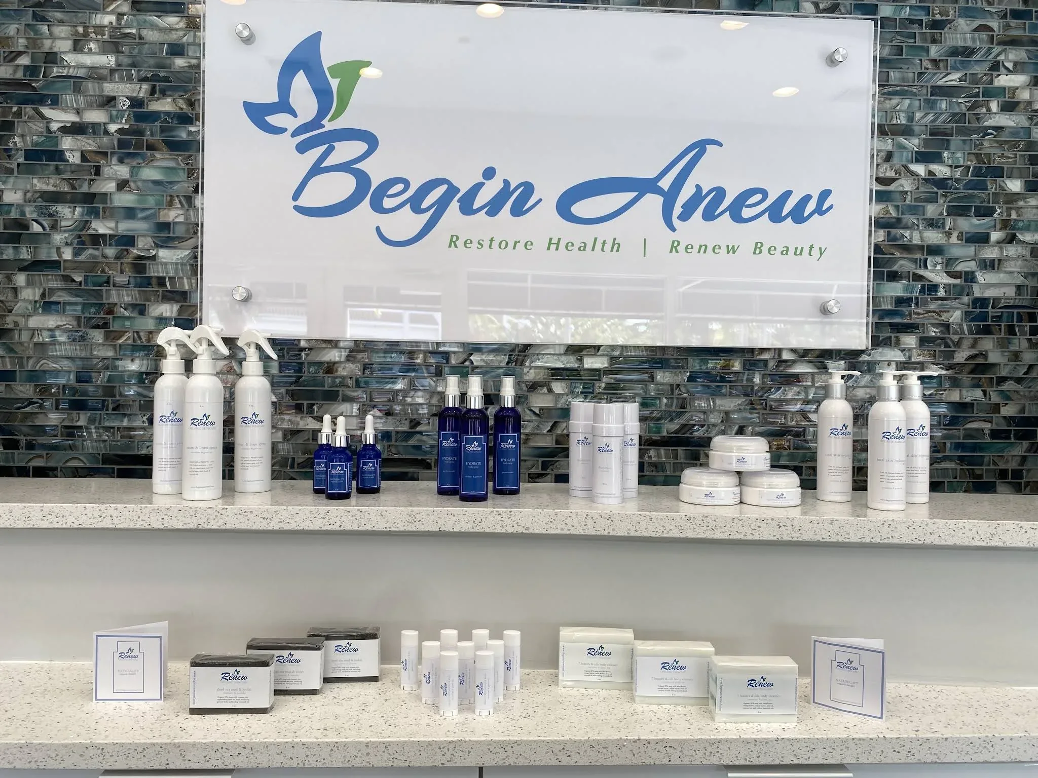 Skincare products beneath a Begin Anew sign on a blue mosaic wall.