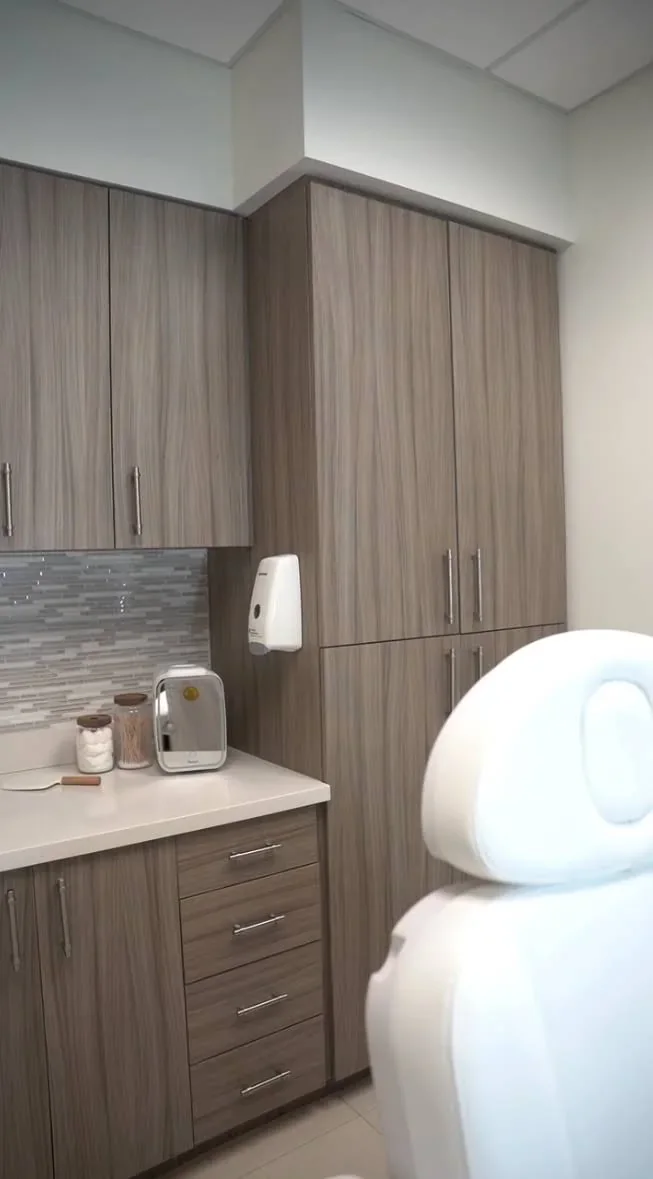 Empty white chair beside woodgrain cabinetry and a tiled backsplash.