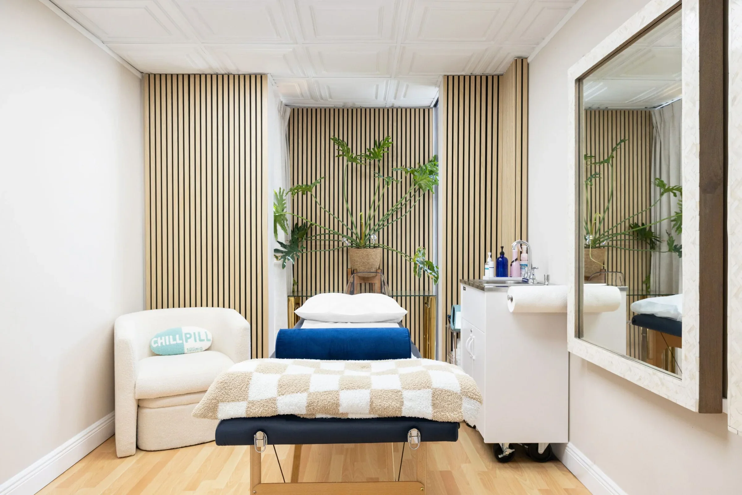 Empty treatment bed, white guest chair, sink cabinet and slatted wood wall.