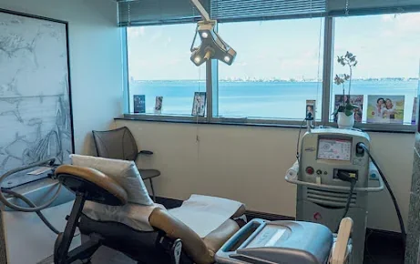 Empty examination room with reclining chair, equipment and a water-facing window.