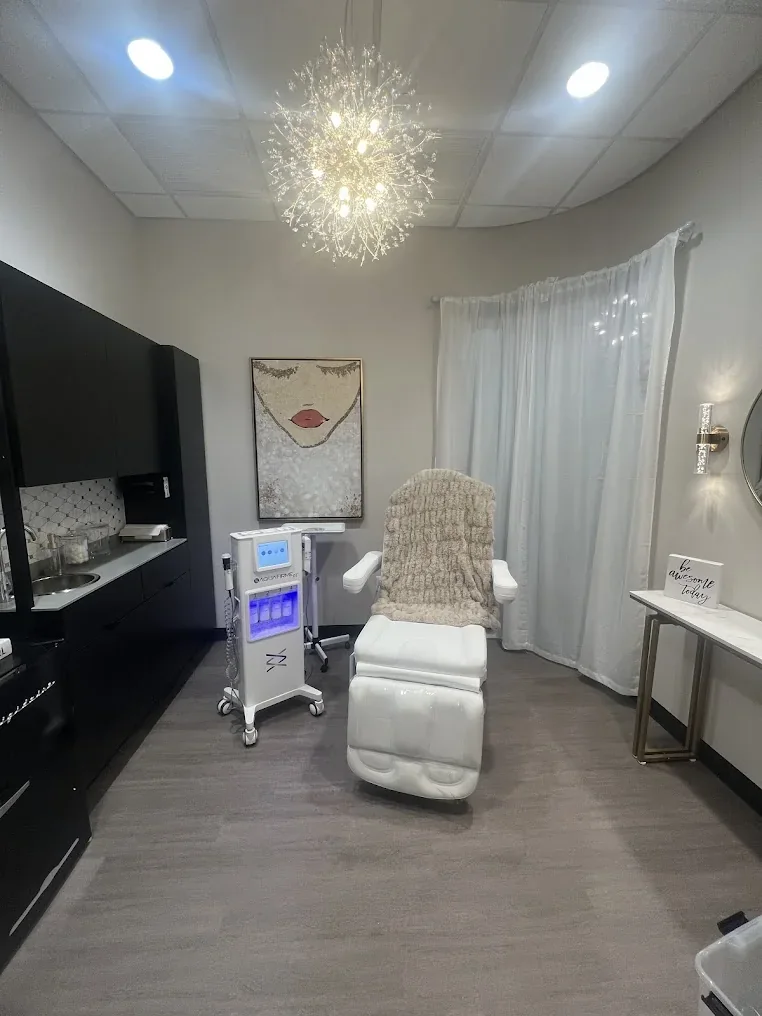 Empty spa room with white reclining chair, dark cabinets, curtained window and chandelier.