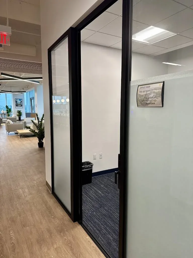 Glass office entry with a Longévité Palm Beach sign beside a shared corridor.