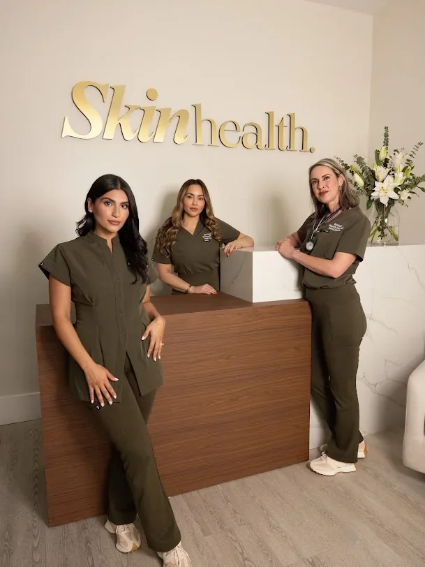 Three team members in matching olive uniforms beside the SkinHealth reception sign.