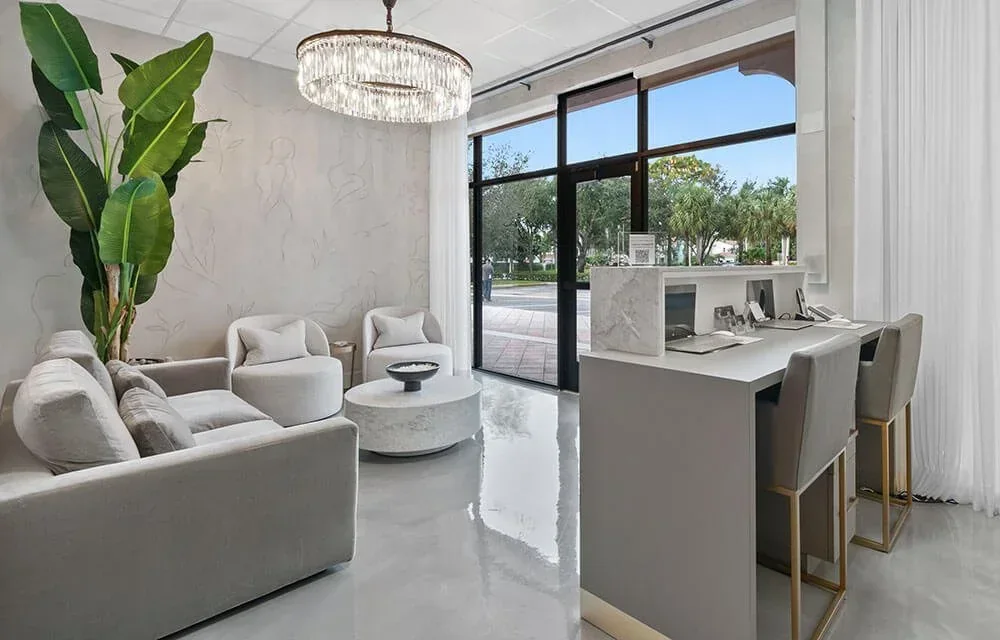 Reception counter, gray seating, chandelier and glass entrance doors.