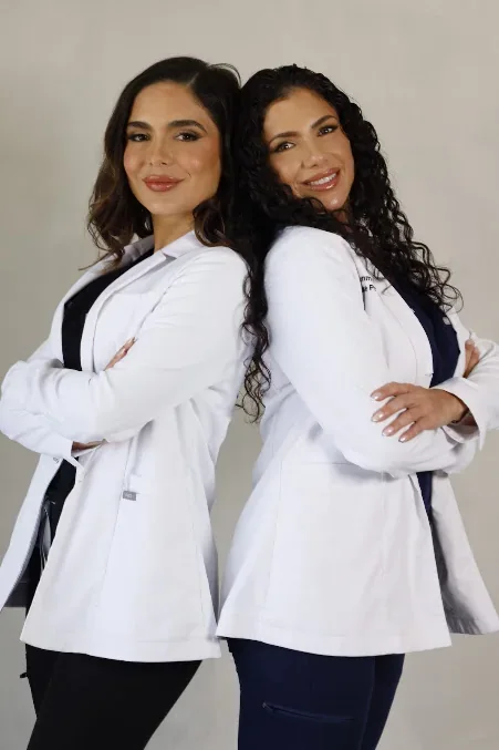 Two clinic team members in white coats posed together against a neutral wall.
