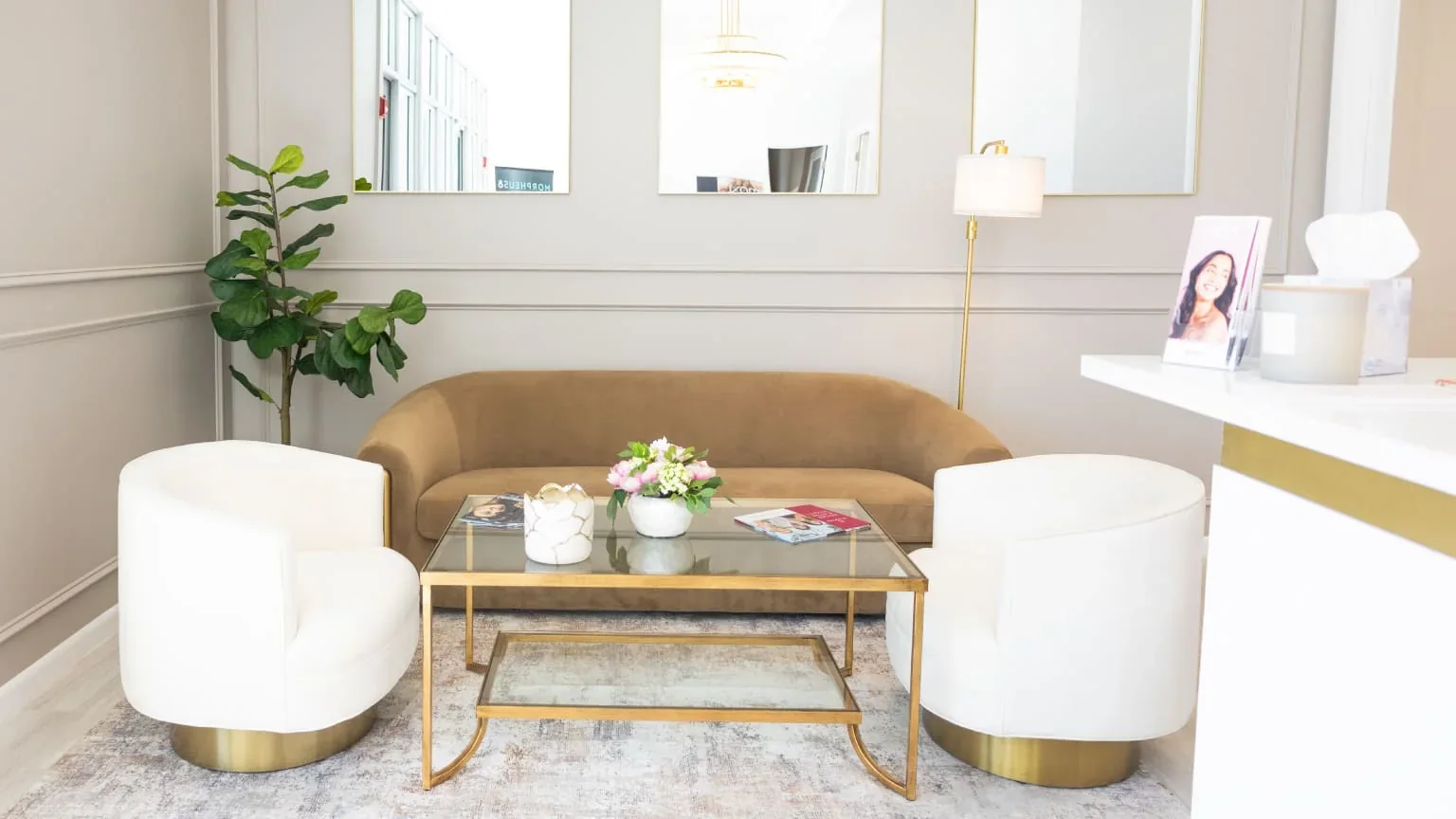 Empty waiting area with a gold sofa, two white chairs and a glass coffee table.
