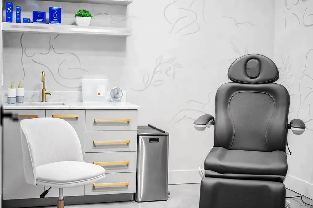 Empty black reclining chair beside a white chair, sink, drawers and product shelf.