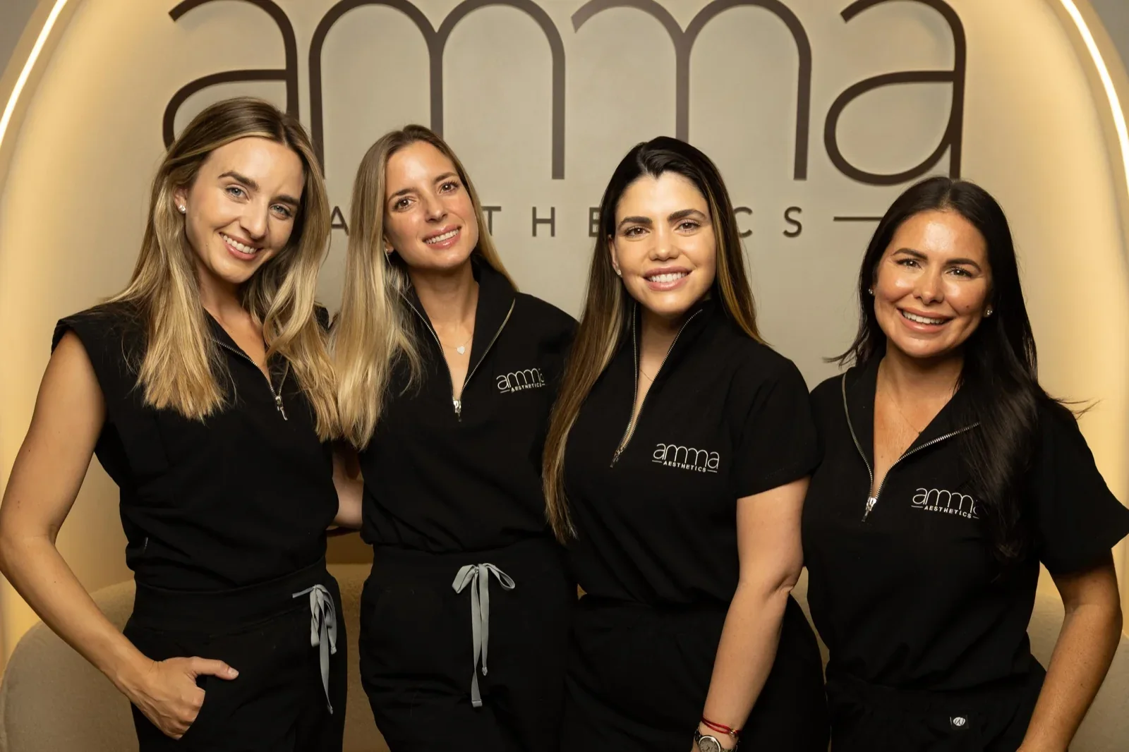 Four team members in black AMMA uniforms in front of the clinic sign.
