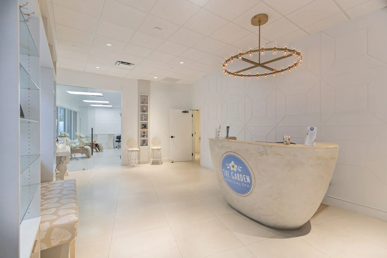 Empty reception with a curved branded desk, chandelier and white patterned wall.
