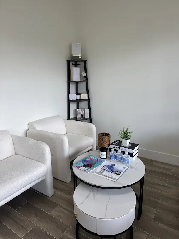 Two white armchairs beside a round coffee table, magazines and a tall corner shelf.
