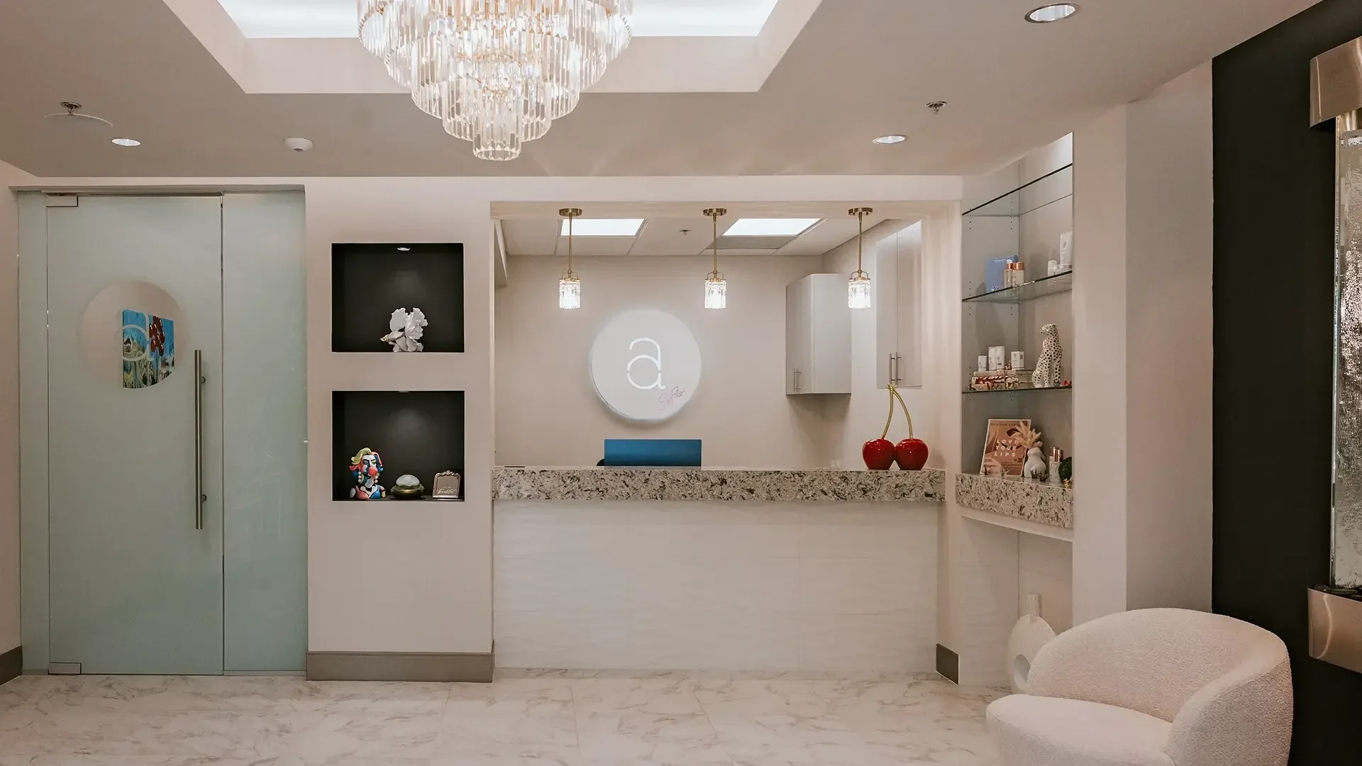 Empty white reception counter, circular Amelia emblem, chandelier and product shelves.