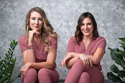 Rachel Polazzi and Jessica Bourgeois seated in matching rose-colored uniforms.