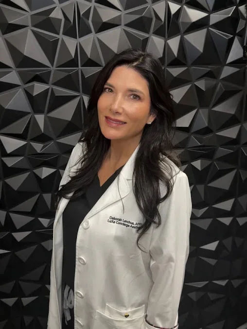 Practitioner in a white LuXe Concierge Aesthetics coat against a geometric wall.