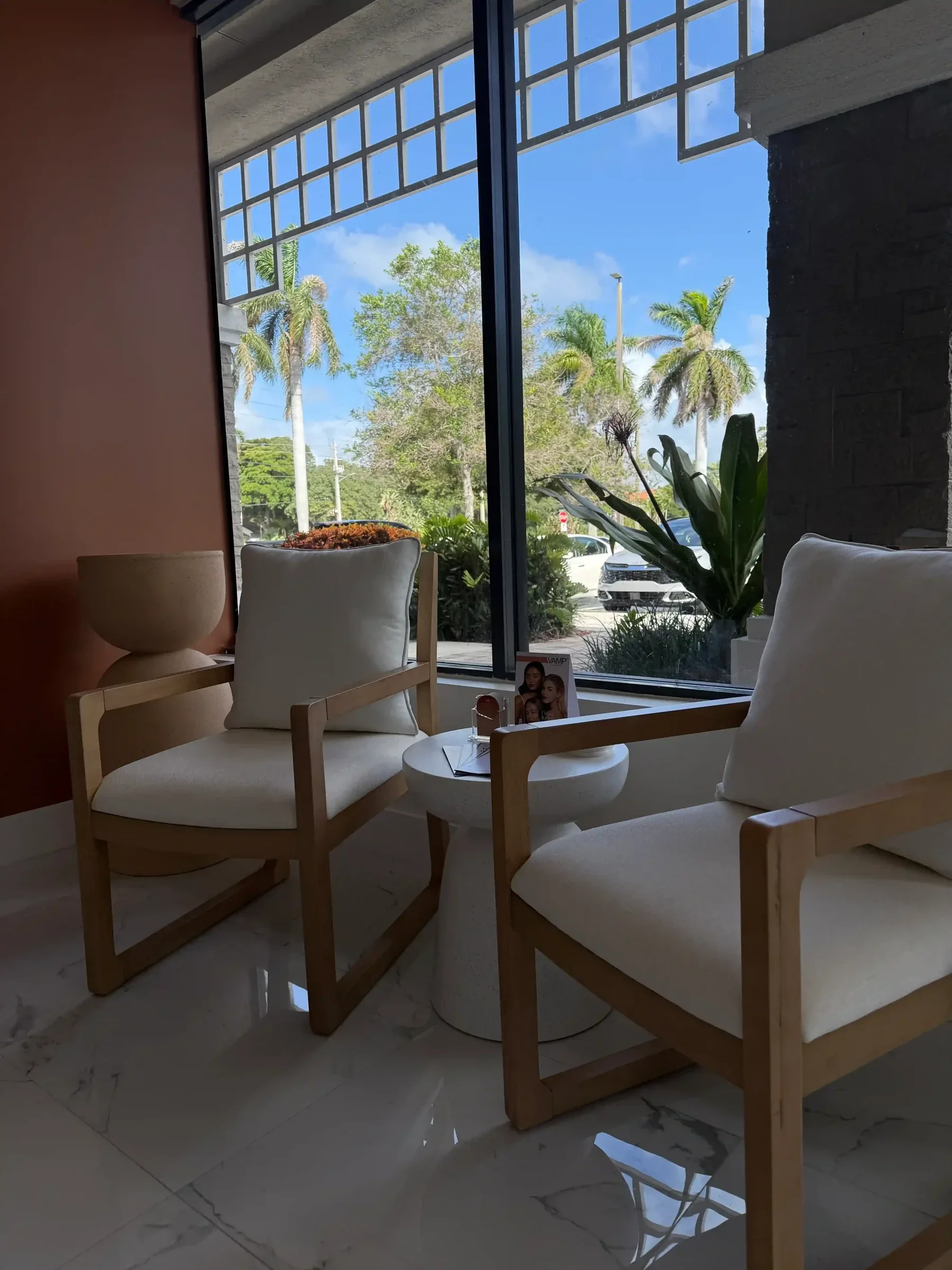 Two empty white-cushioned wooden chairs beside a large window.