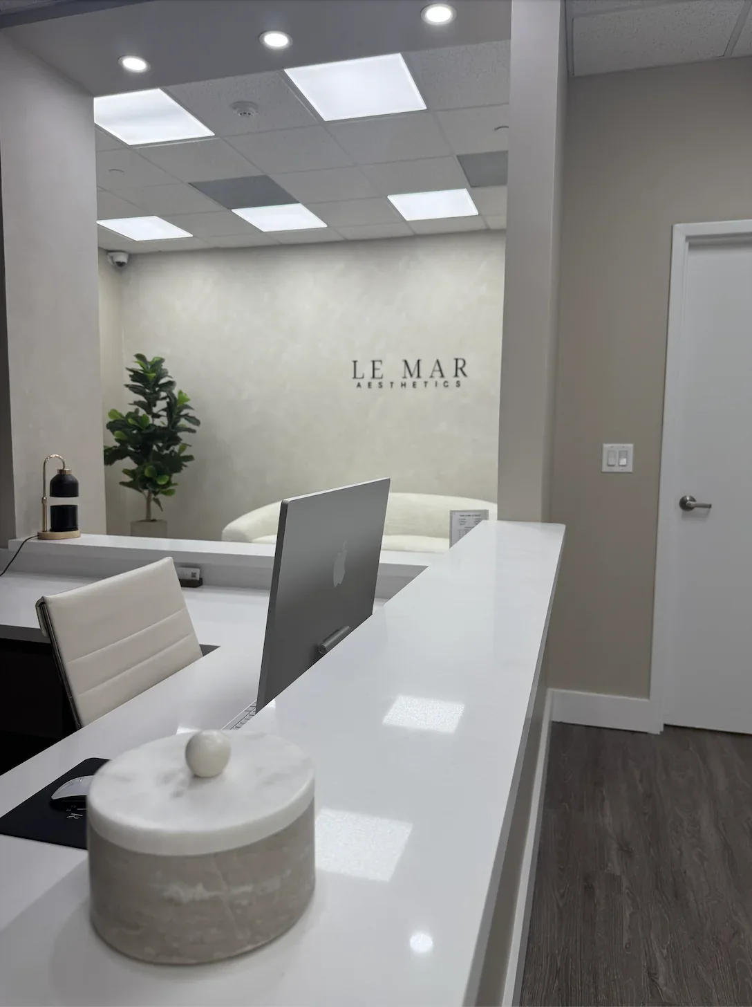 White reception counter with a computer facing away and Le Mar wall lettering behind.