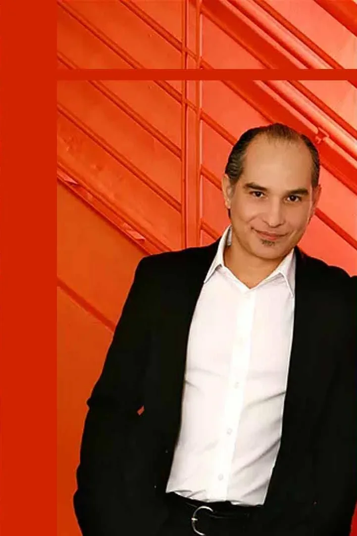 Eduardo Ayub wearing a dark jacket and white shirt against an orange background.