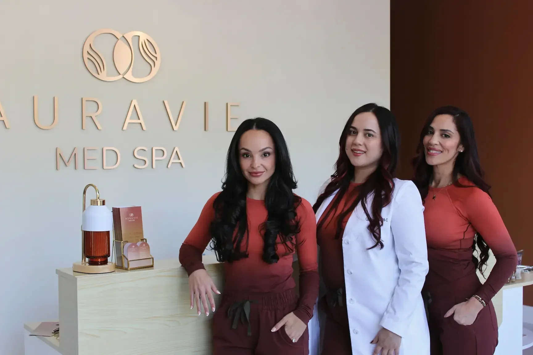 Three team members posed beside the Auravie Med Spa reception sign.