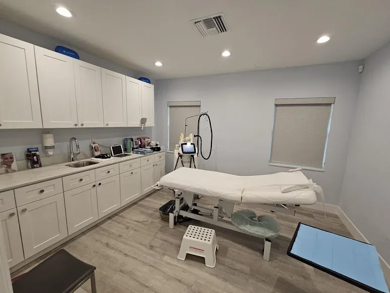 Empty treatment room with white cabinetry, covered adjustable bed and equipment.