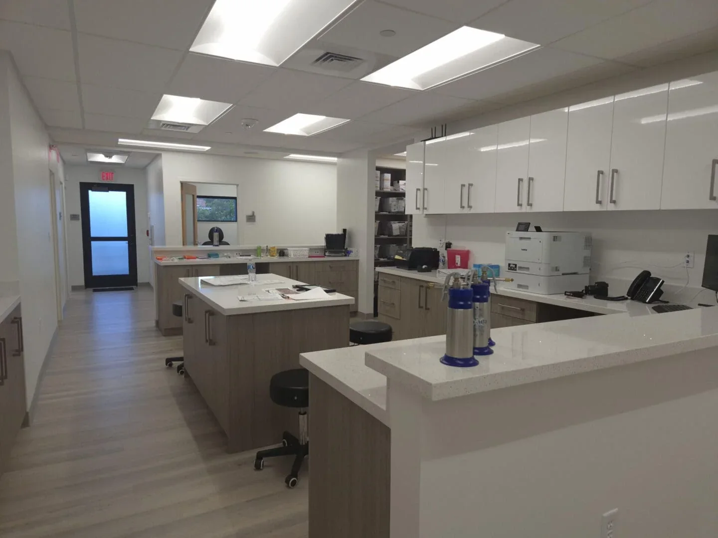 White storage cabinets, counters, a central worktop and stools in an empty office work area.