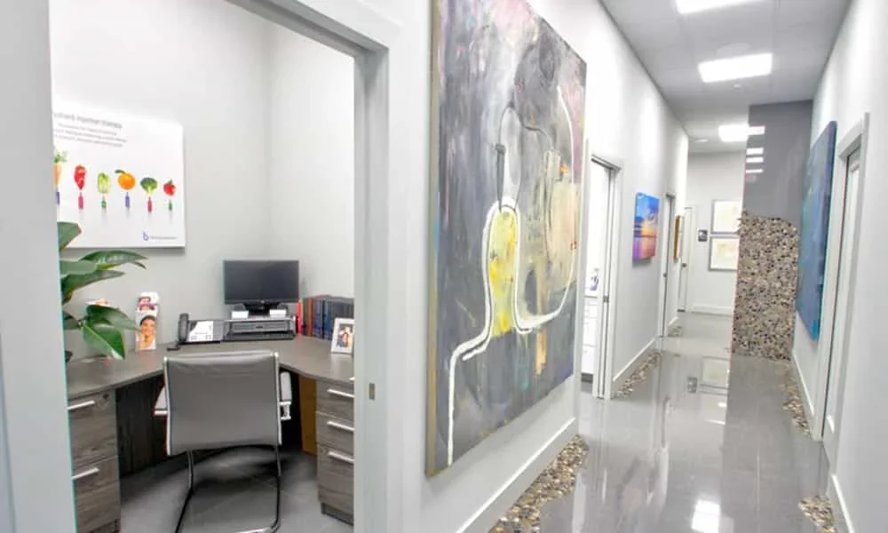 Empty office opening into a hallway, with artwork and a dark monitor.