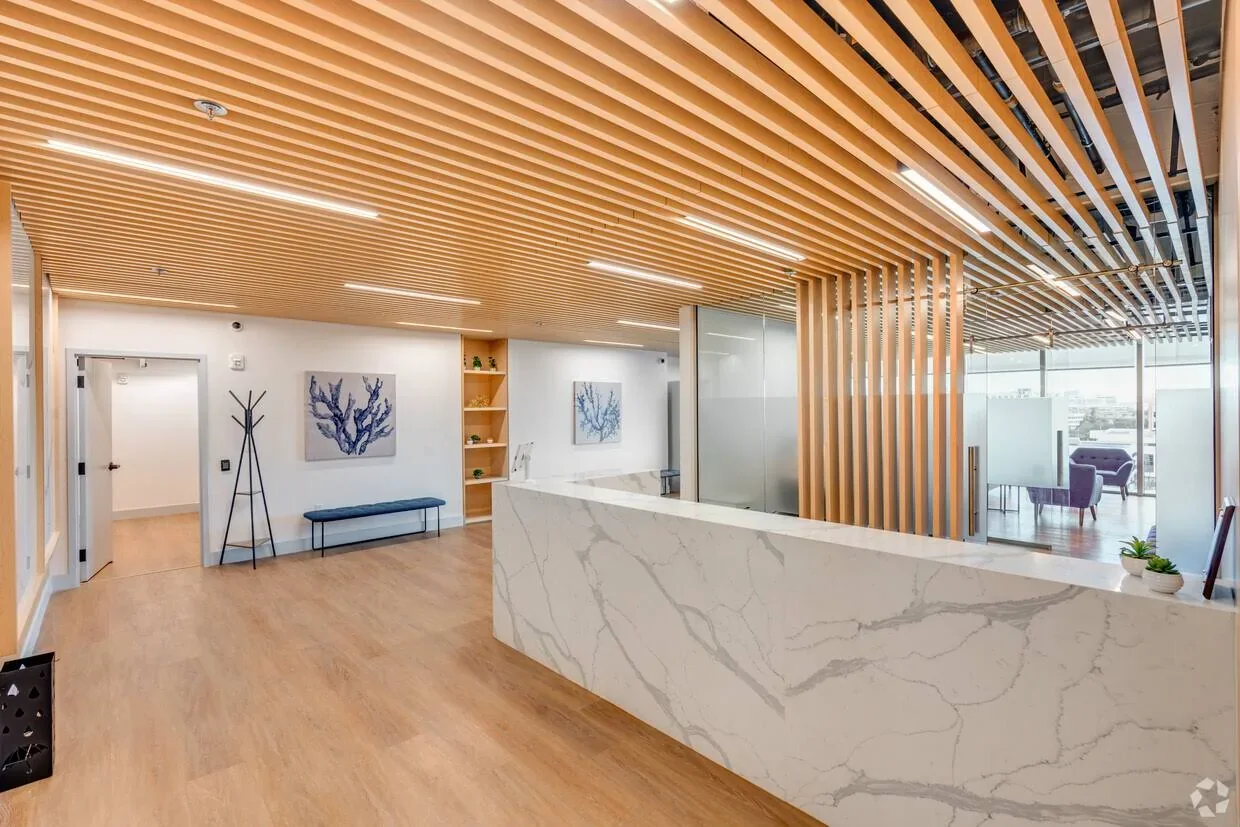 Empty reception with a marble-patterned counter, wood slat ceiling and glass office partitions.