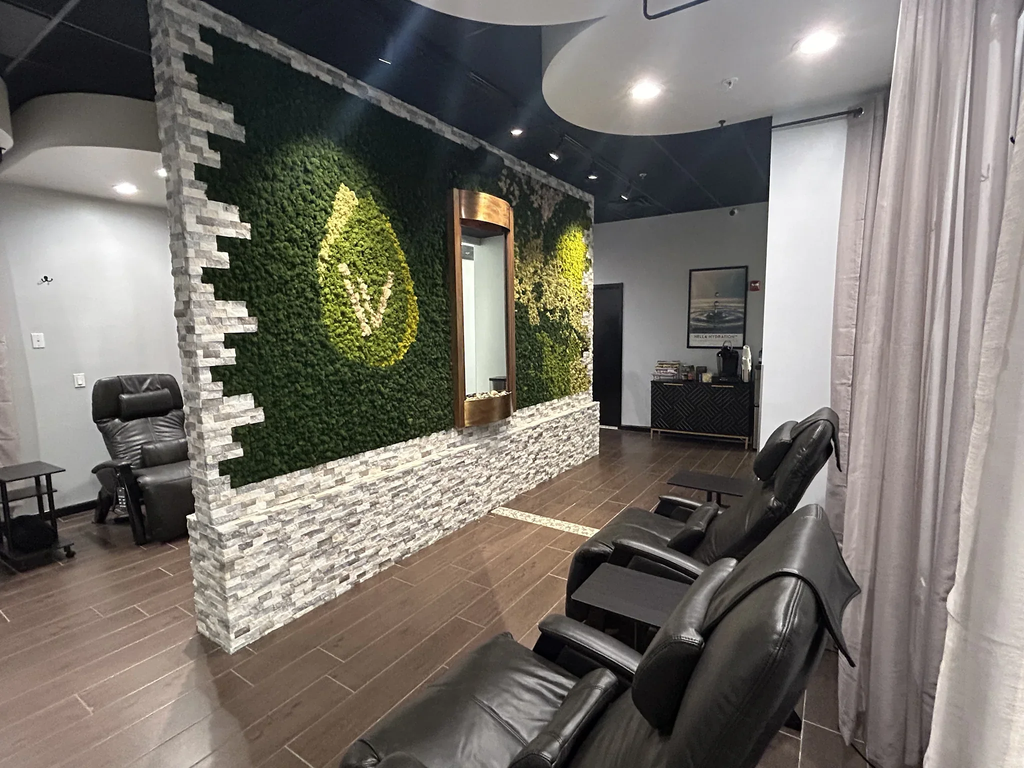 Empty black reclining chairs beside a green moss droplet partition and stone accent wall.