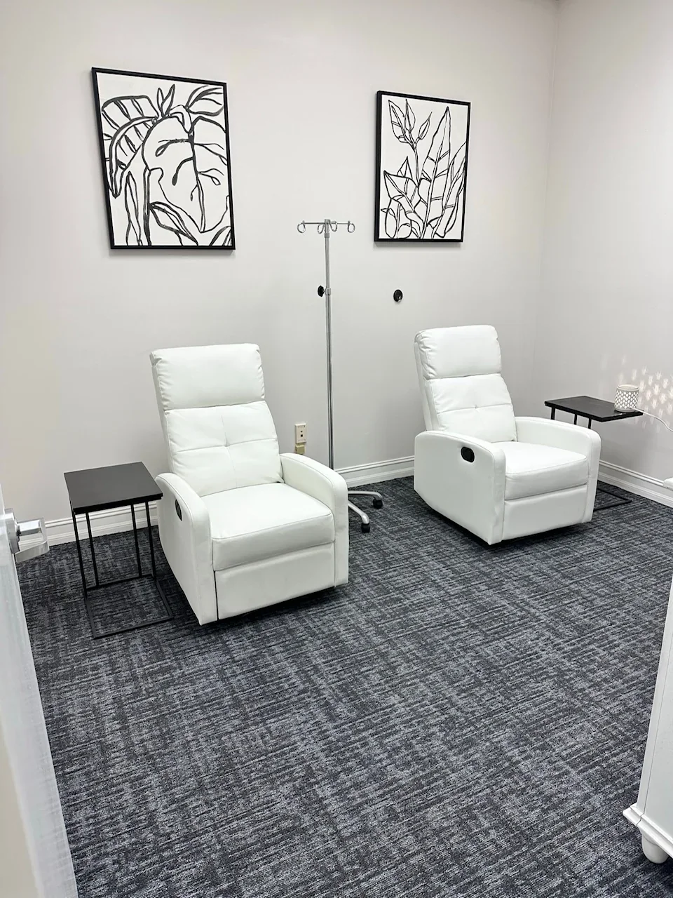 Empty room with two white recliners, side tables and botanical wall art.