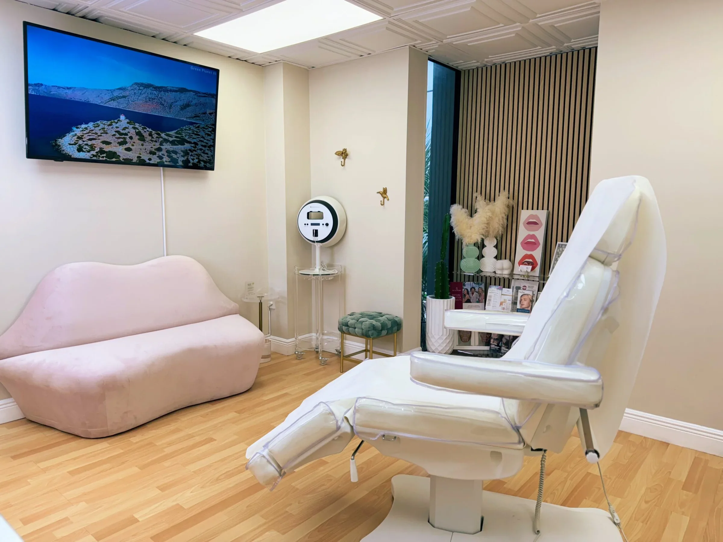 Empty white examination chair beside a pink sofa, television and green stool.
