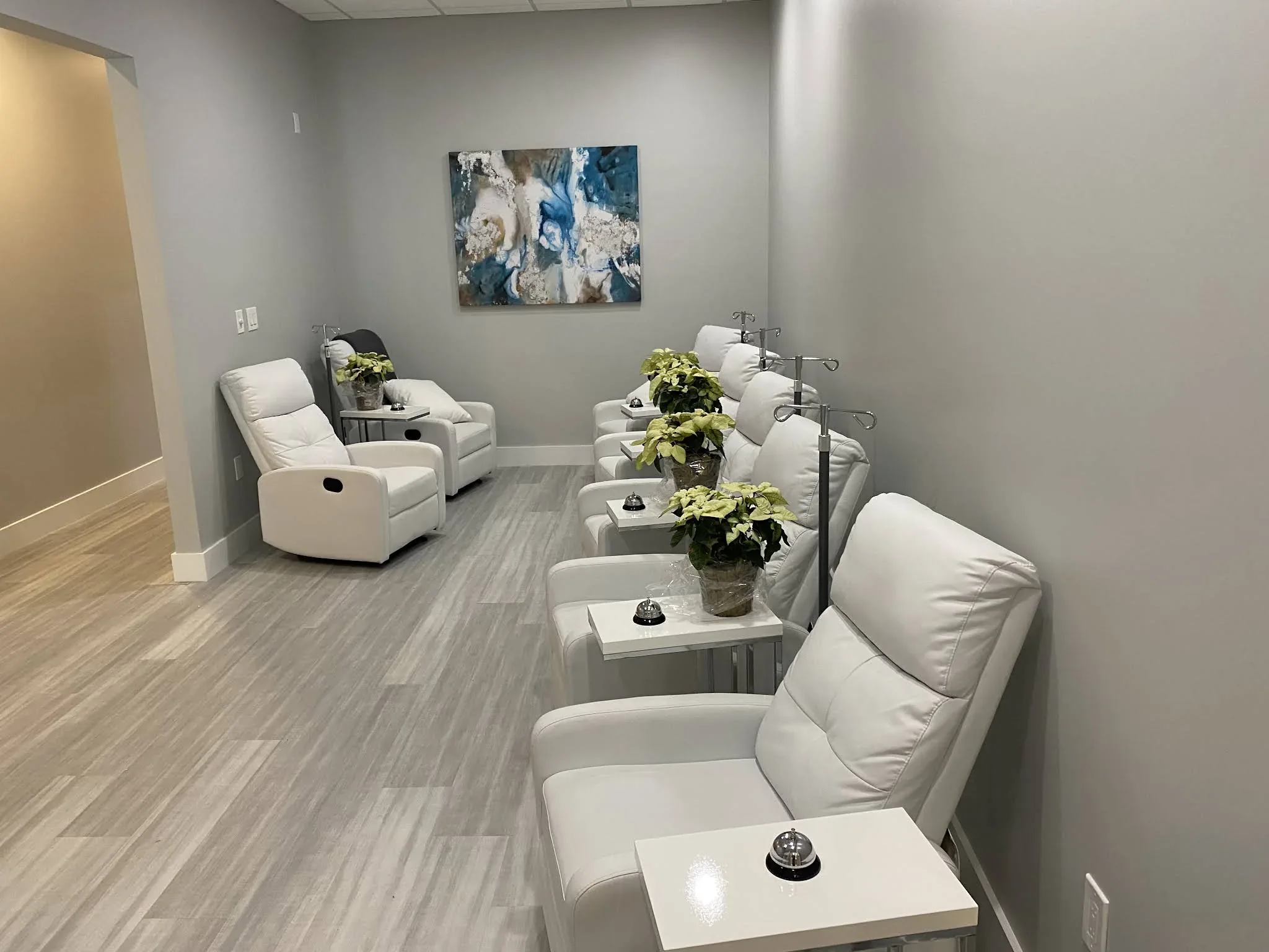 Rows of empty white reclining chairs, small tables and plants in a gray room.