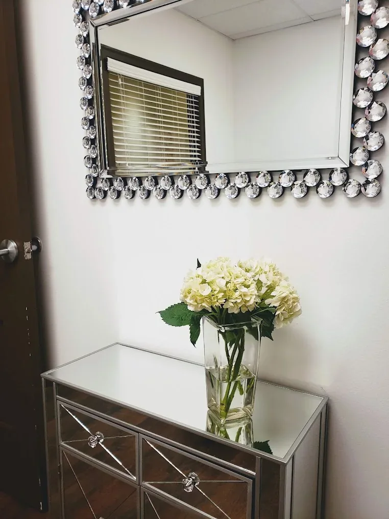 Mirrored console with white flowers beneath a decorative mirror in a small empty room.