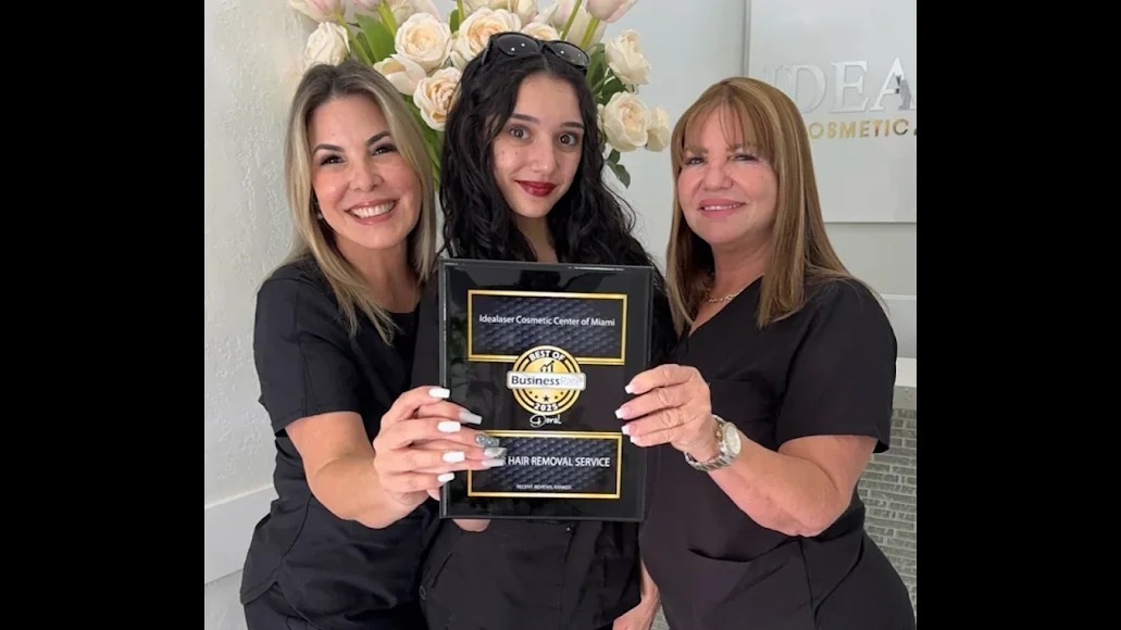Three team members in dark uniforms holding a business recognition plaque in front of IdeaLaser signage.