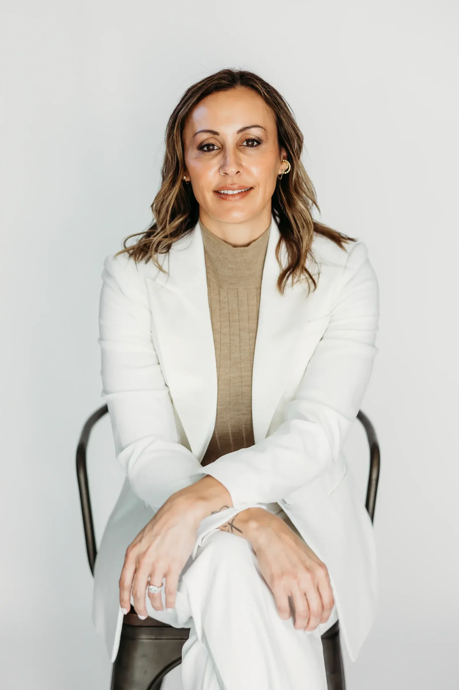 Nicole Capodieci seated in a white suit against a plain wall.