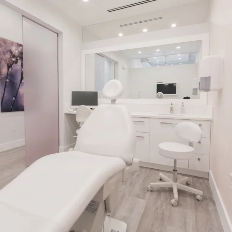 Empty white reclining chair beside a stool, cabinetry, dark monitor and large wall mirror.