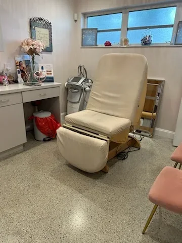 Unoccupied room with a cream reclining chair, white cabinets, windows and unused equipment.