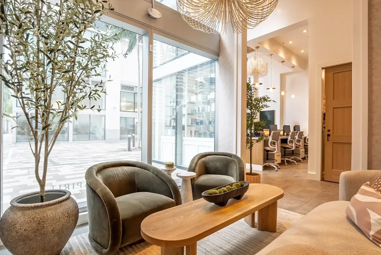 Green lounge chairs, wood table and large storefront windows.