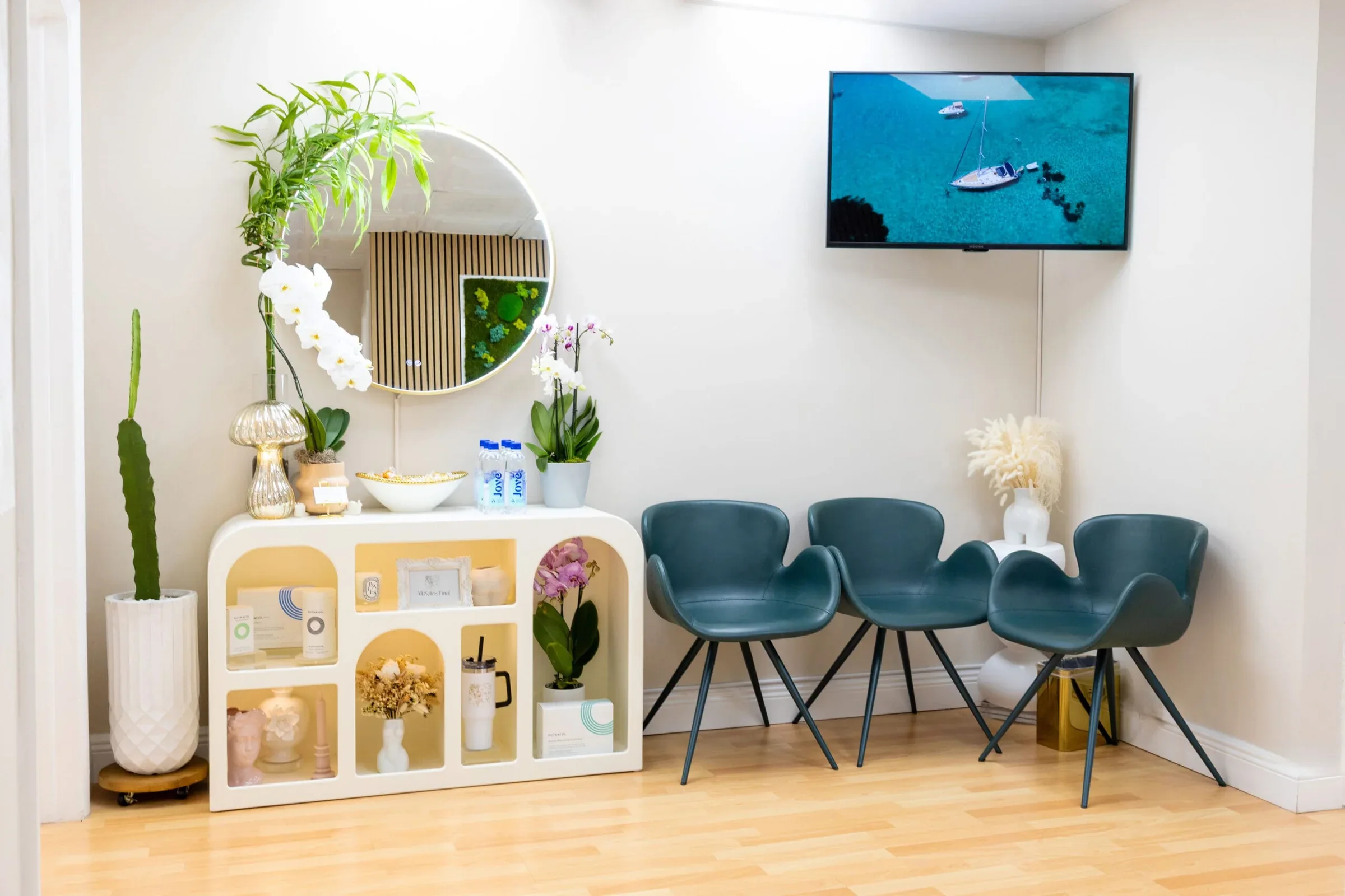 Four teal chairs beside a white refreshment console and round mirror.