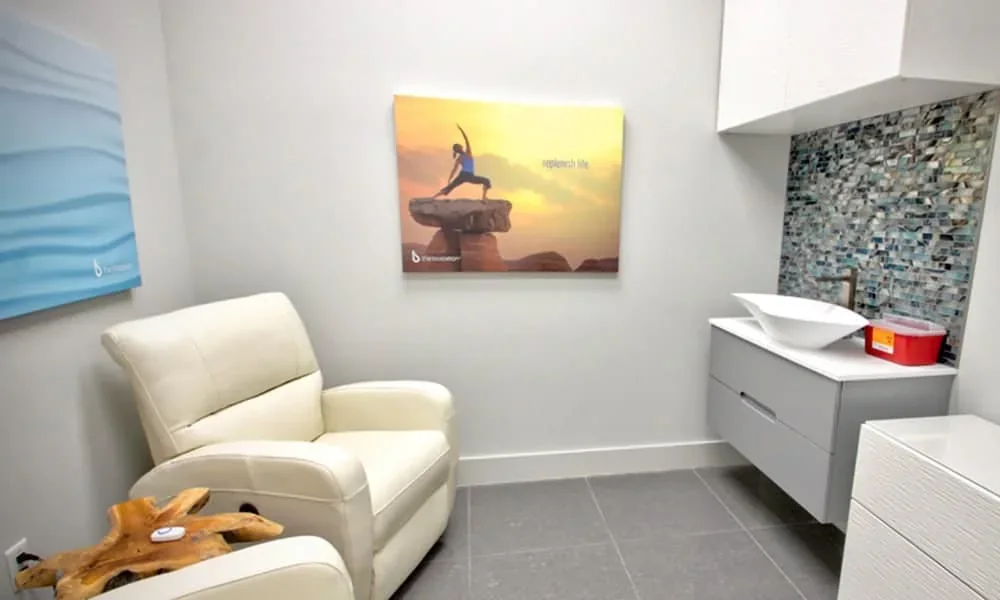 Empty treatment room with a reclining chair, sink, cabinets and wall art.