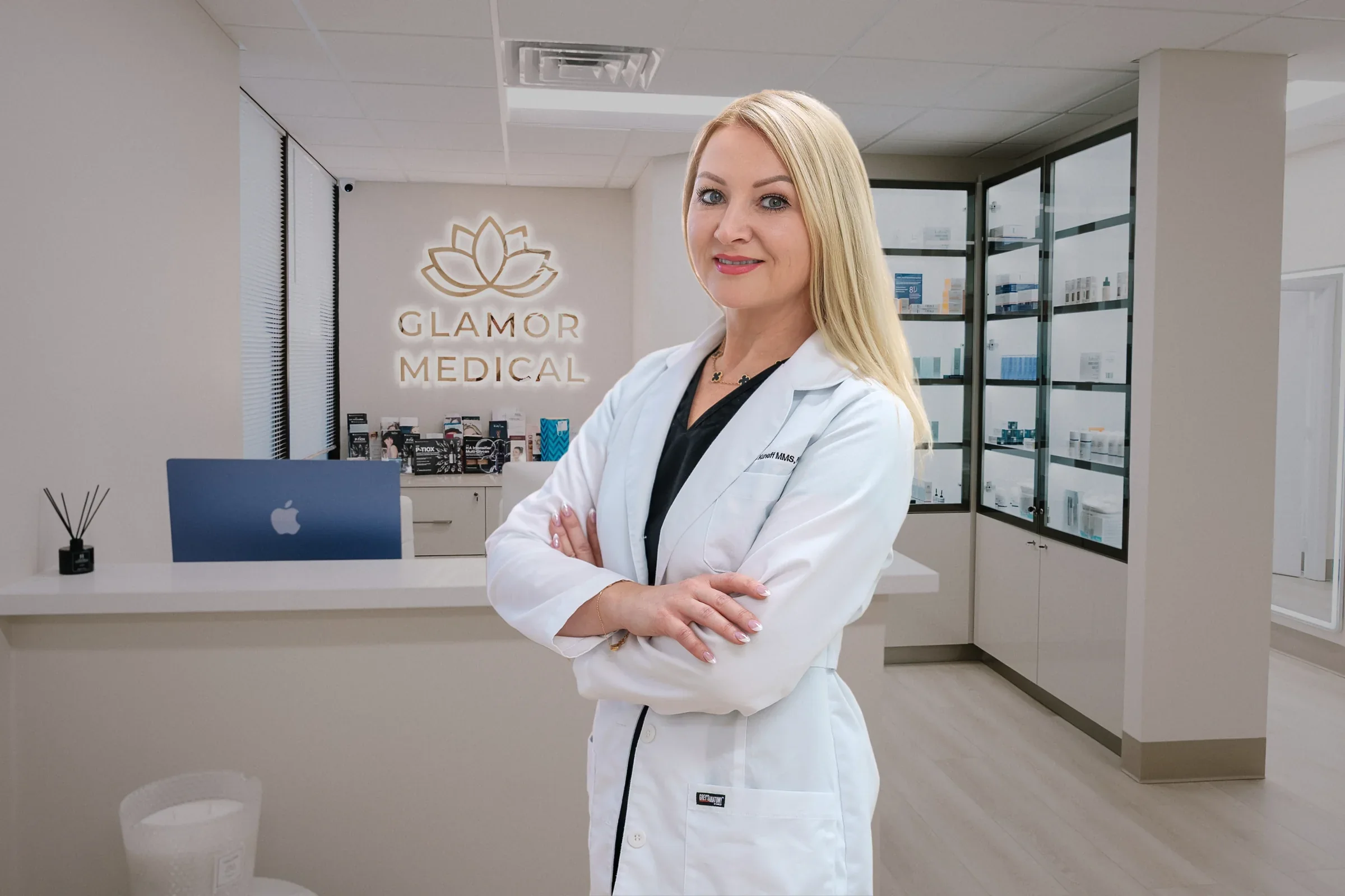 Practitioner in a white coat standing in front of Glamor Medical wall signage and product cabinets.