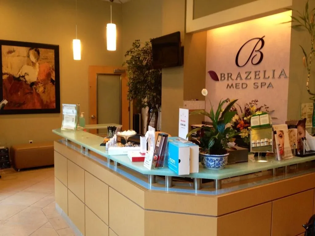 Empty glass-topped reception with plants, brochures and a Brazelia Med Spa wall sign.