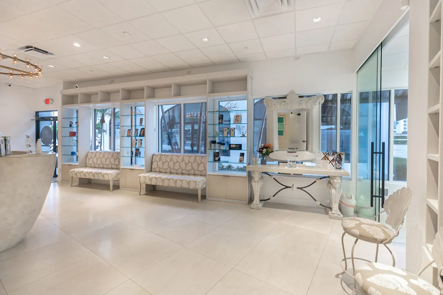Empty waiting area with patterned benches, glass display shelves, windows and a decorative mirror.