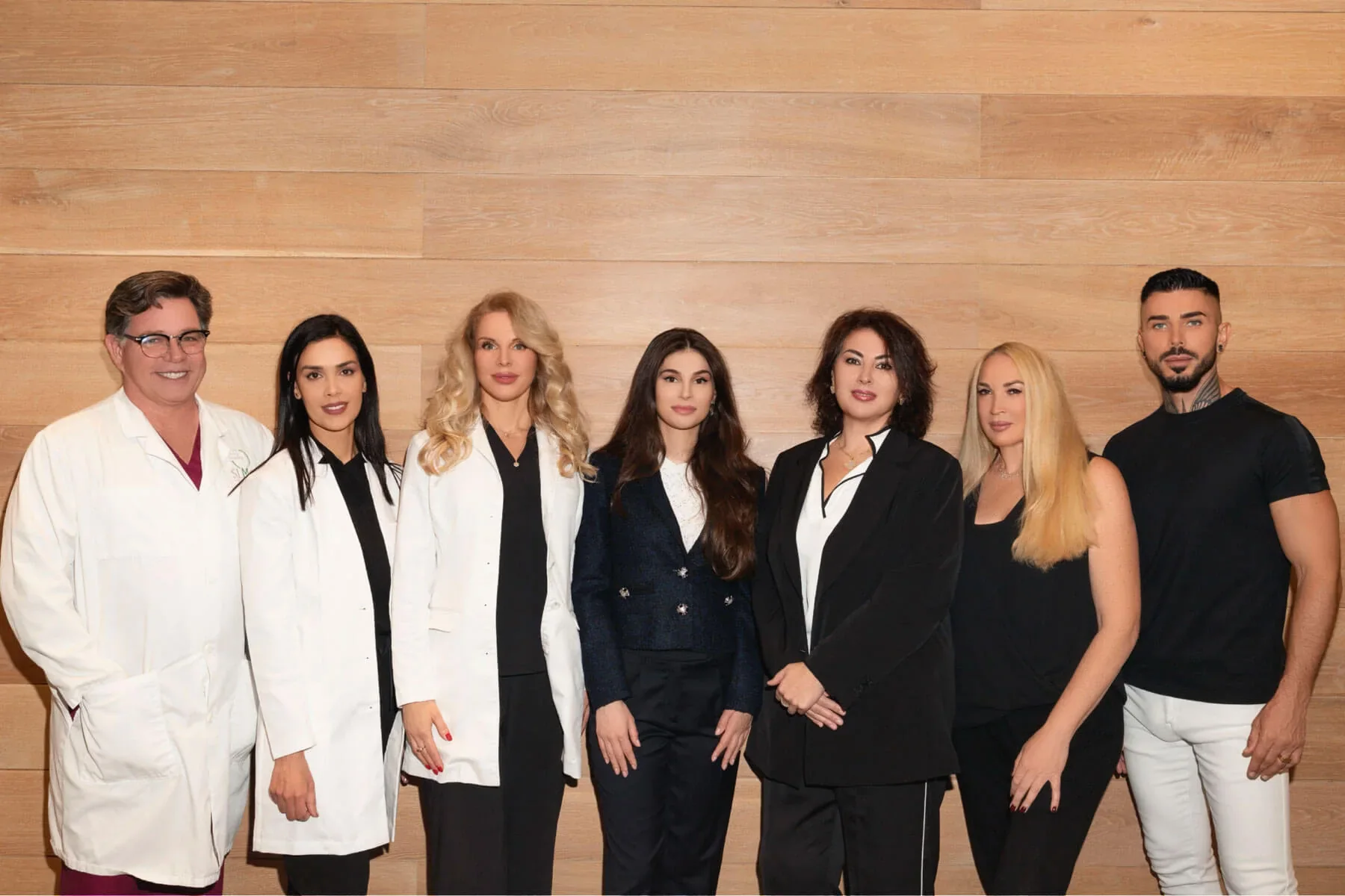 Seven Unique Clinic team members posing together against a wood-paneled wall.