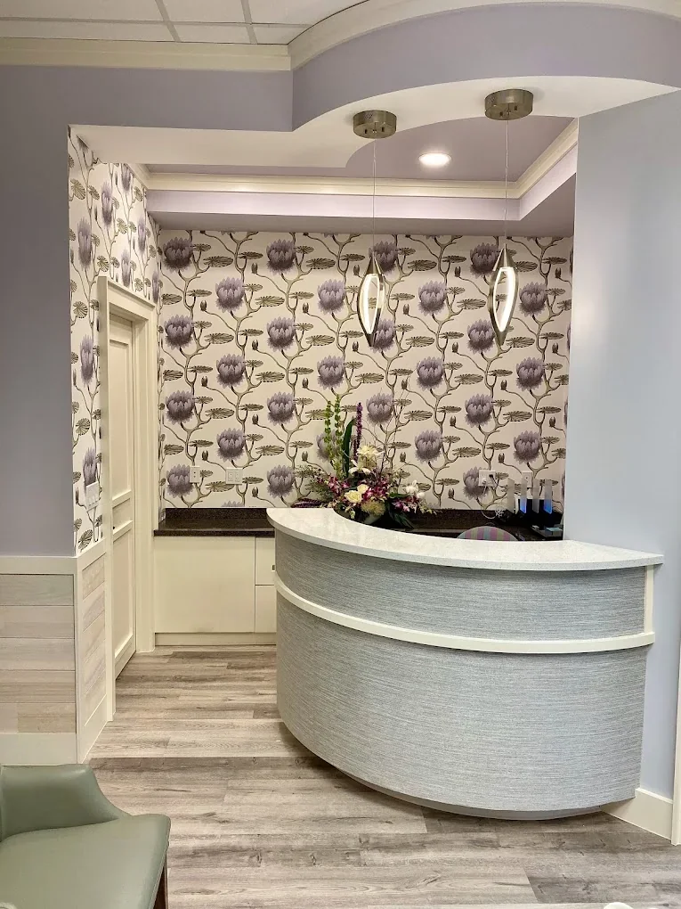 Empty reception area with a curved gray desk, purple floral wallpaper and pendant lights.